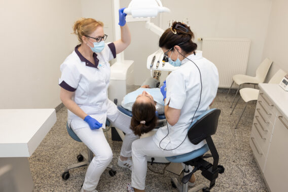 Assistant shines lamp on patient's teeth in chair - Dental Clinics Oudenbosch