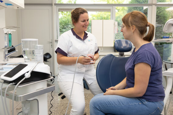 Dentist shows teeth and instrument to patient - Dental Clinics Oudenbosch