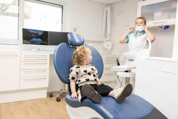 A toddler is sitting in the dental chair and looking at the dentist at Dental Clinics Reeshof