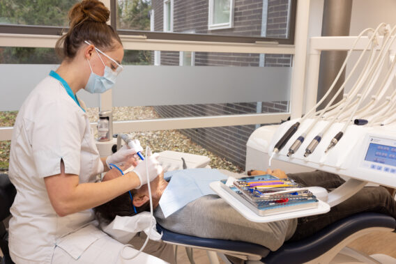 Behandelaar behandelt patiënt die in stoel ligt - Dental Clinics Ermelo