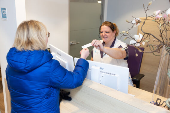 Receptiemedewerker overhandigt patiënt een afsprakenkaartje bij de receptie Dental Clinics Zeewolde