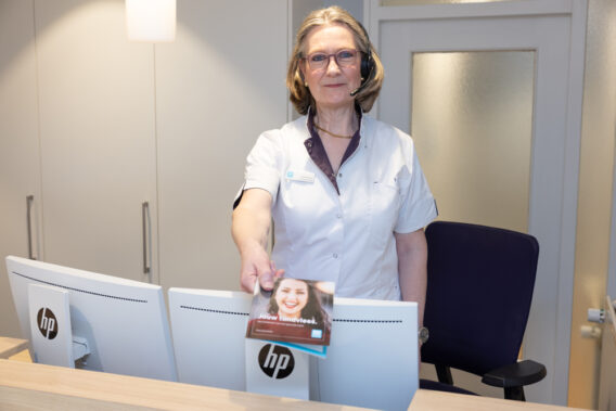 Receptionist geeft folder 'Jouw tandvlees' aan patiënt mee