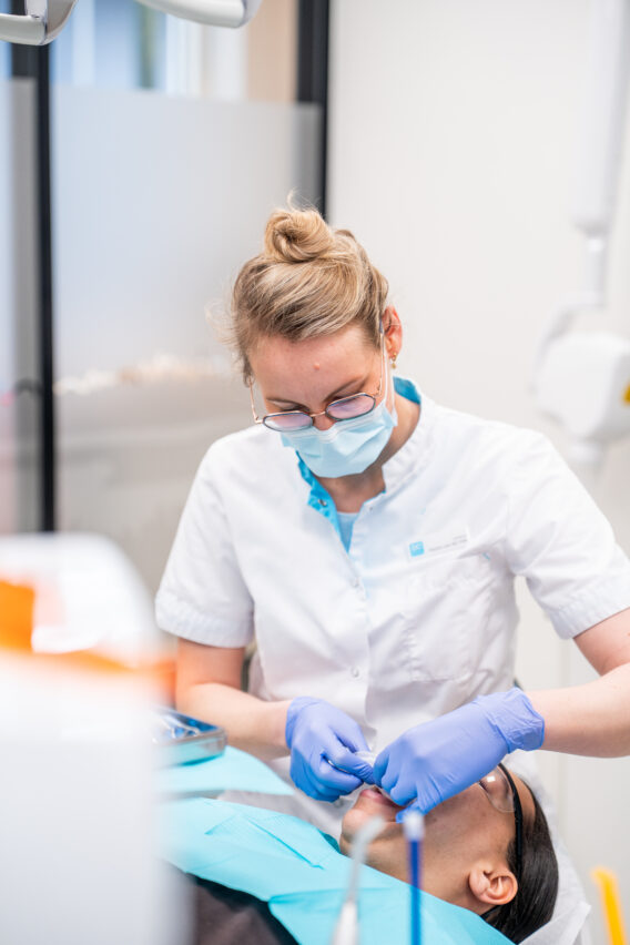 Behandelaar kijkt naar mond van patiënt terwijl haar handen een instrument vasthouden Dental Clinics Gieten