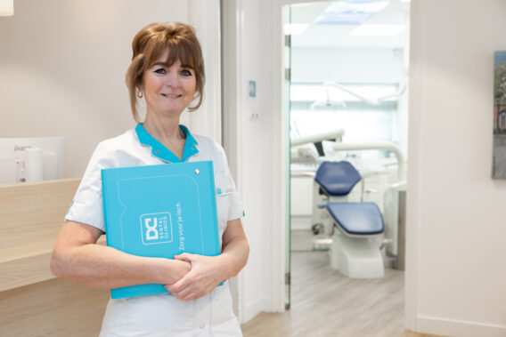 Assistent met blauwe zorgmap bij de ingang van een behandelkamer Dental Clinics Purmerend Weidevenne