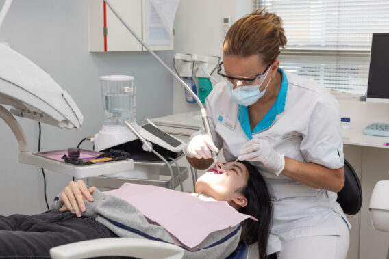 Assistent houdt instrumenten in mond van patiënt in stoel Dental Clinics Purmerend Weidevenne