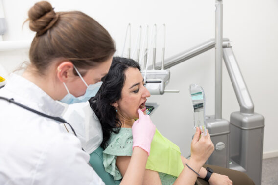 Patiënt bij Dental Clinics kijkt in handspiegel naar plek in mond aangewezen door tandarts
