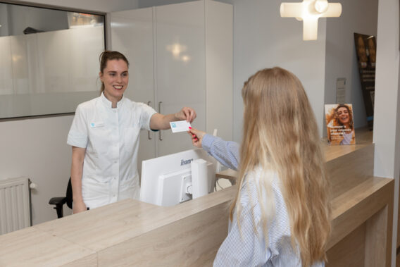 Receptionist geeft afsprakenkaartje aan patiënt