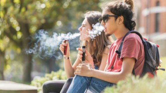 Twee studenten zitten naast elkaar te vapen op de universteitscampus