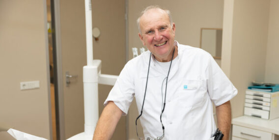 Tandarts-directeur Eric Muller leunt tegen stoel en lacht in camera Dental Clinics Hattem
