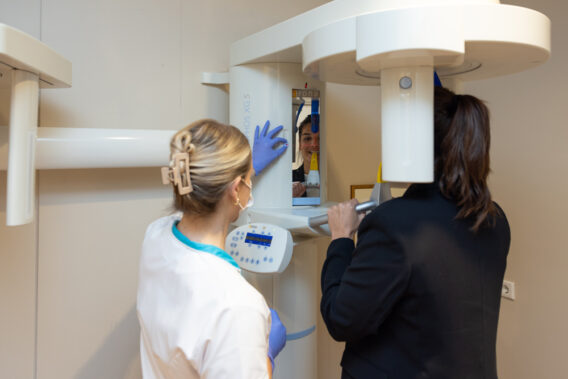 Tandartsassistent draait aan knopje van röntgenapparaat waar patiënt in staat Dental Clinics Hattem