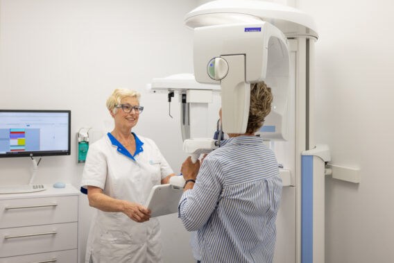 An assistant helps a patient into the X-ray machine at Dental Clinics